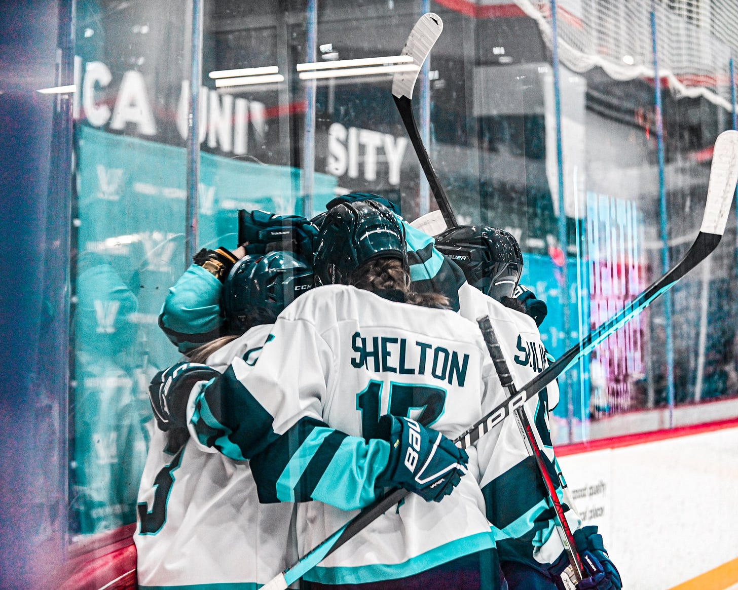 Players for the PWHL New York team huddling together to celebrate a goal.