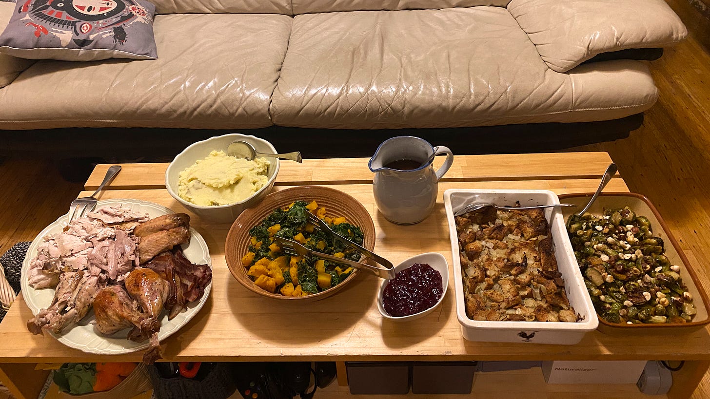 Arranged on a rectangular coffee table are serving dishes of turkey, mashed potatoes, kale & squash, cranberry sauce, gravy, stuffing, and brussels sprouts. 