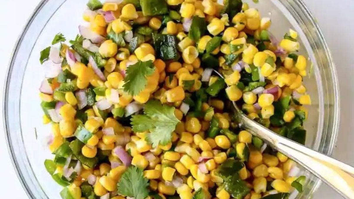 A fresh corn salad with chopped cilantro, diced jalapeños, and red onions mixed together in a clear glass bowl, viewed from above.