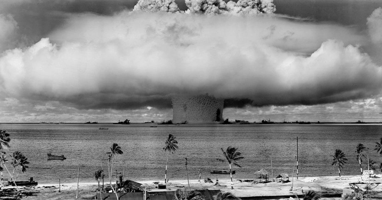 Picture of a beach in black and white witha  nuclear explosion mushroom cloud off in the distance