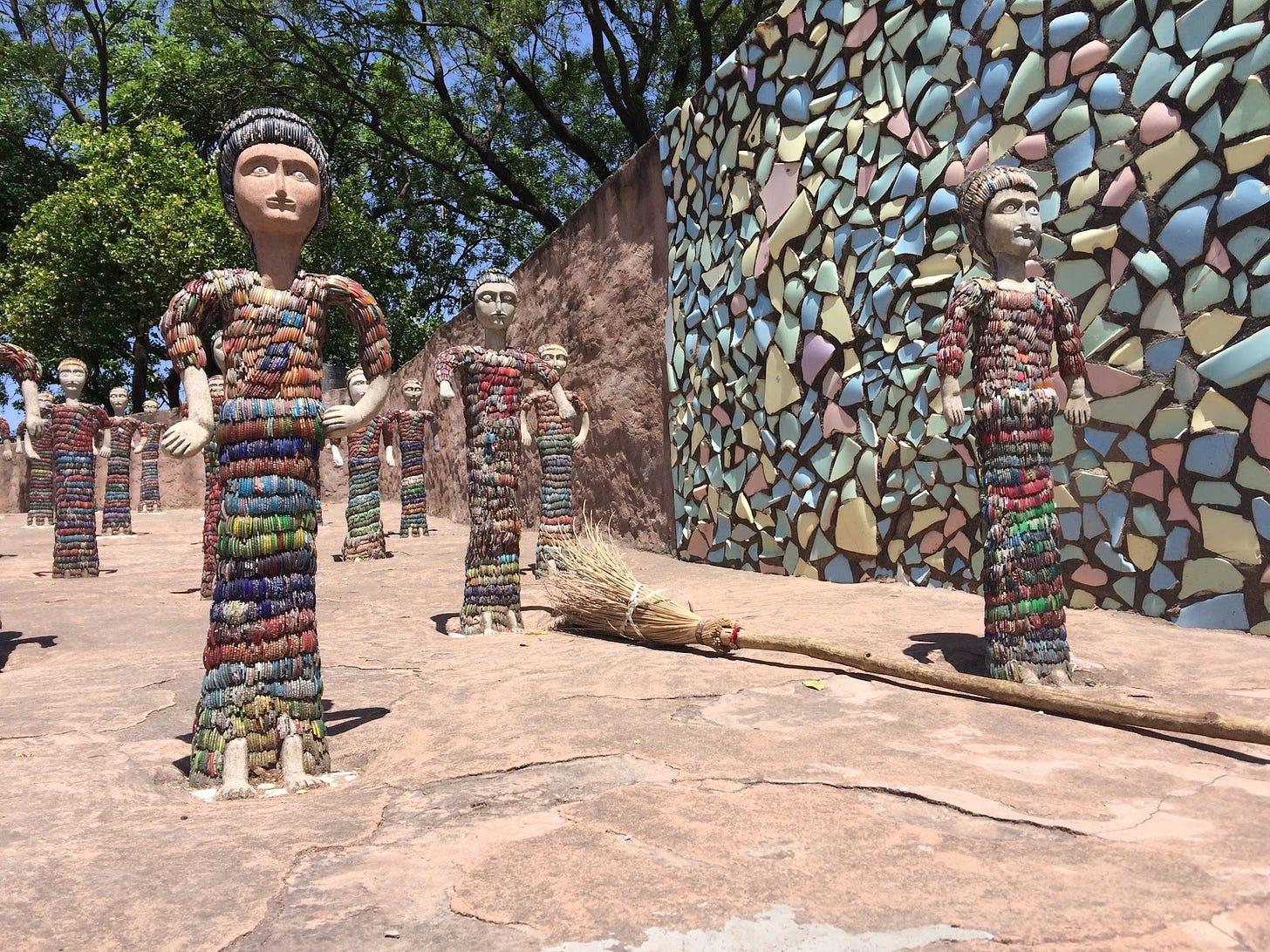 Photograph of a Rock Garden and open air art space in India. In the frame, you see several sculptures that are roughly three feet tall, made from waste materials such as broken bracelets and bangles in addition to clay