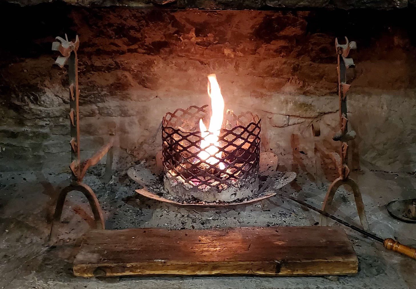 a small flame burns in a metal cage inside a stone hearth