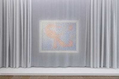 View of an artwork that is obscured by a white curtain that has a description of the work printed on it. 