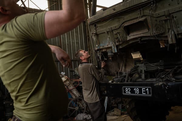 People in a workshop repairing a military transport vehicle.