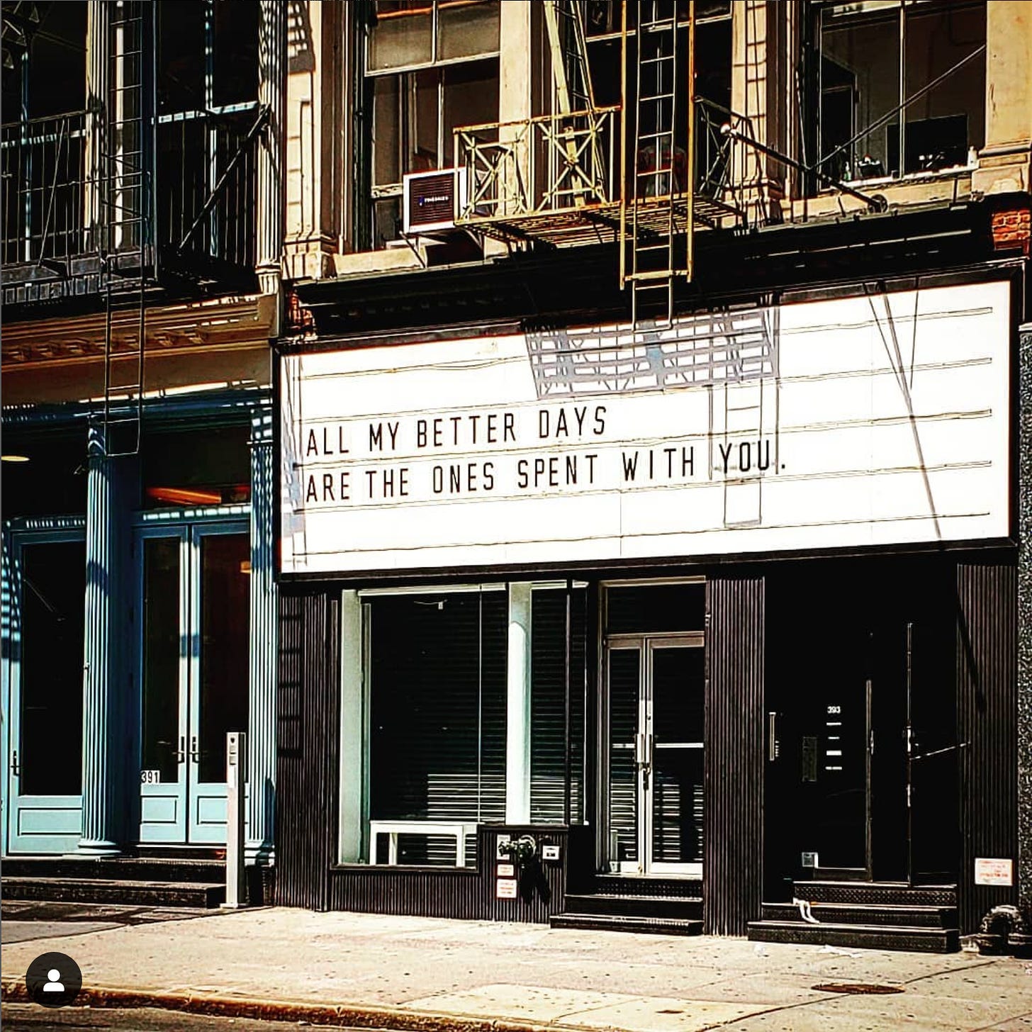 Multi-use building with many doors, windows, and fire escape ladders. A reader board says, "All my better days are the ones spent with you."