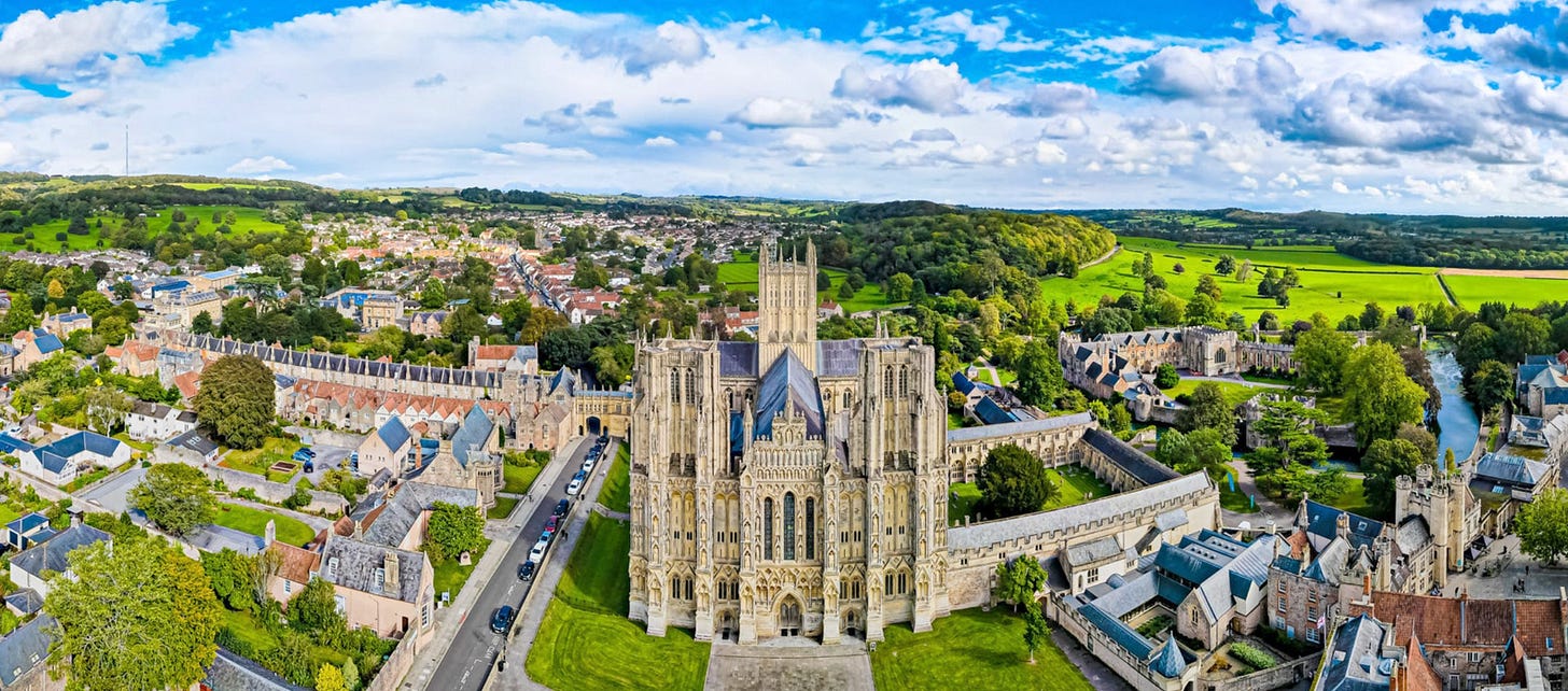 Picturesque Wells, UK. You can see the row of houses that make up the Close on the left, Wells Cathedral in the center, and the Bishop’s Palace and garden on the right of this panorama photo from Wells.co.uk.