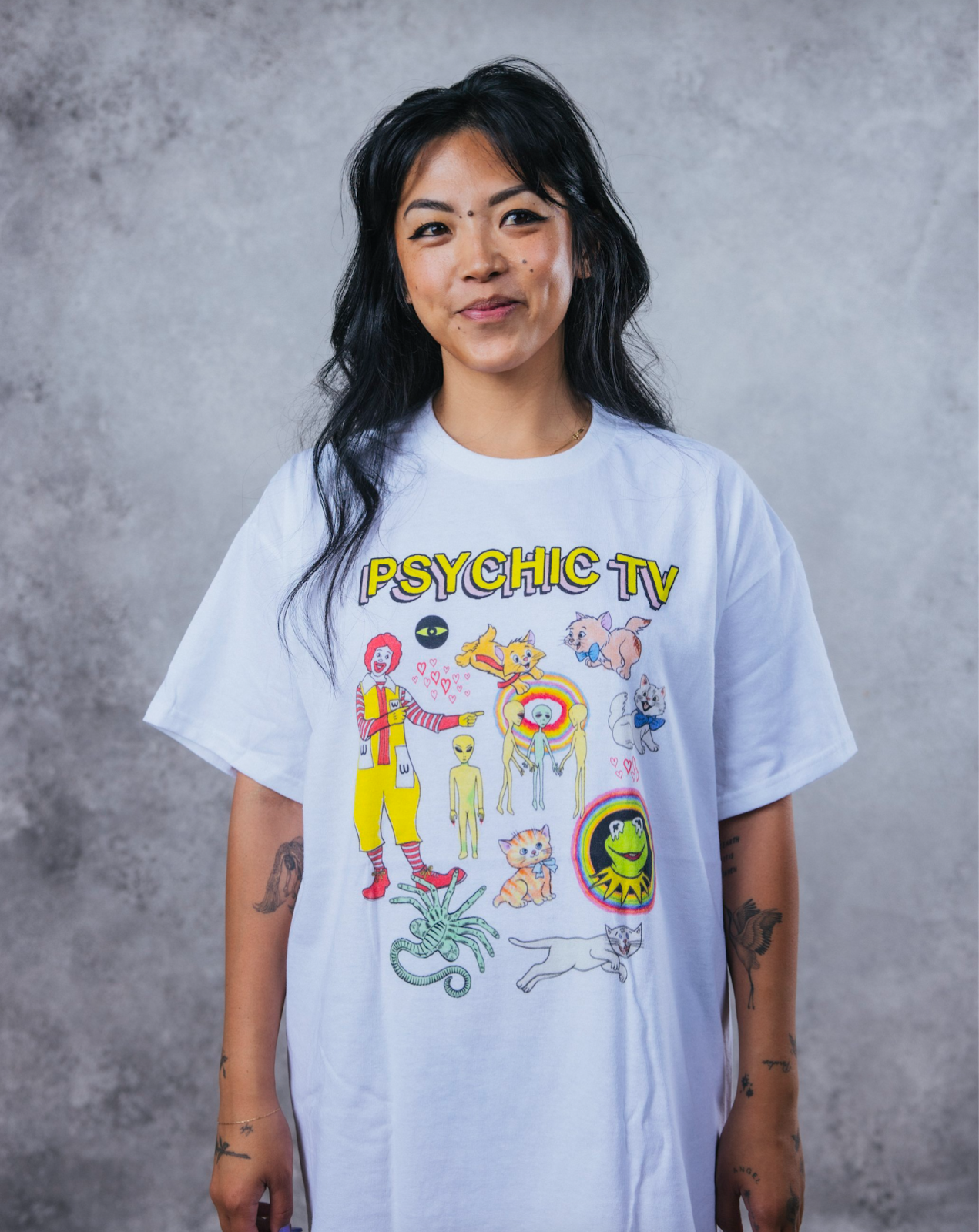 Woman wearing a PHYCHIC TV blue shirt with various bits of weird pop culture on it