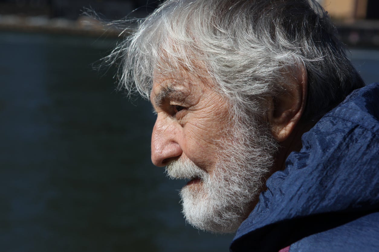 Tight side-view of aging white man with trimmed gray beard and full head of straight gray hair. 