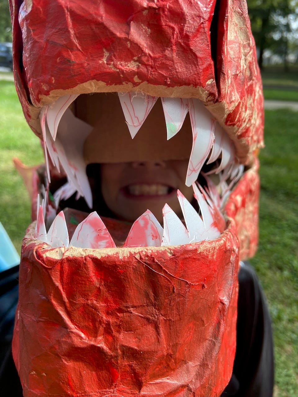 Child wearing a dragon mask in an outdoor class play.