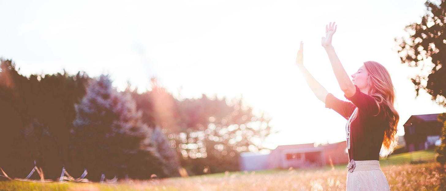 woman hands up in front of green meadows