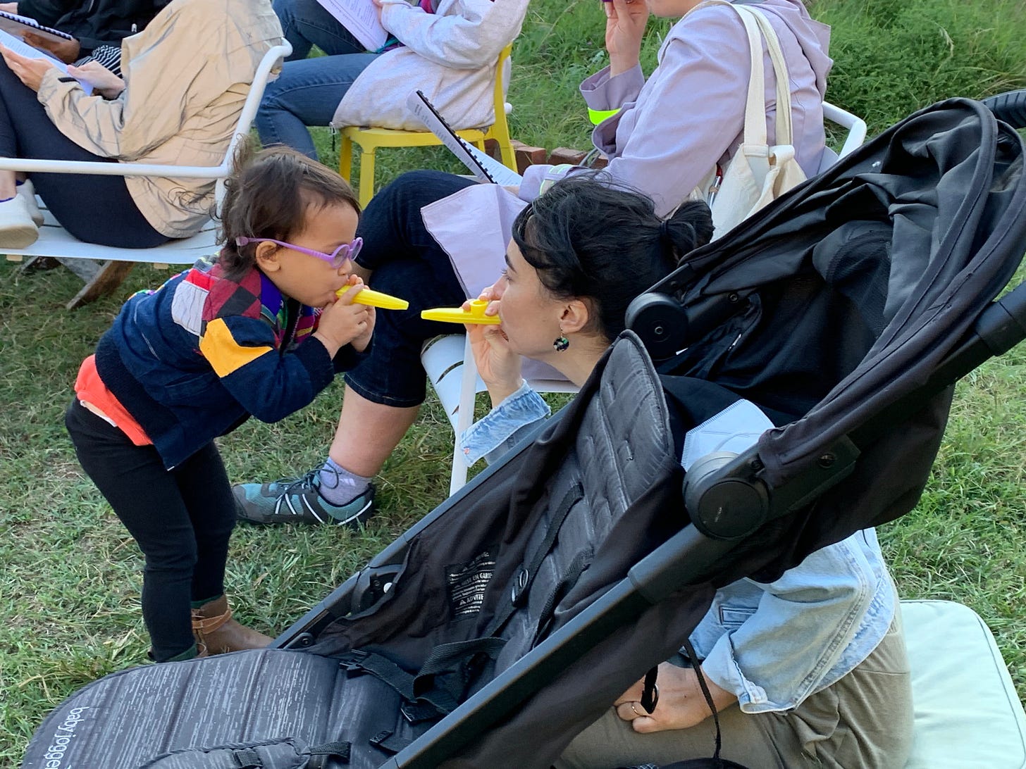 A woman and her toddler sweetly kazoo to each other, face to face, at a sing-along.