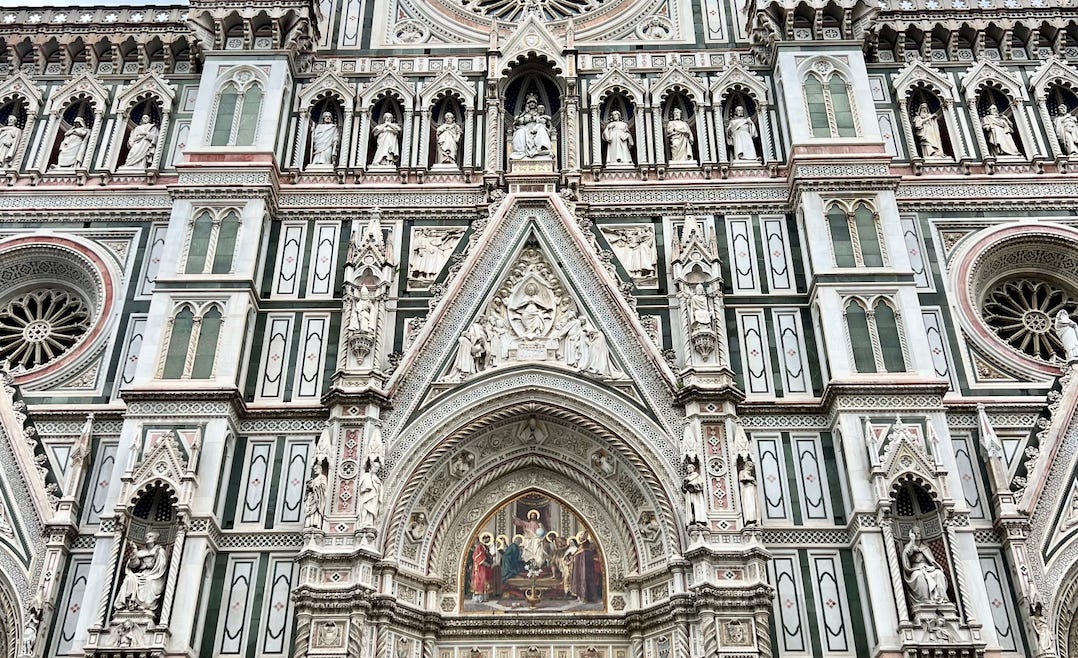 Image of Santa Maria del Fiore, the cathedral in Florence, Italy, which is comprised of colorful marble, many statues, and swathes of intricate art.