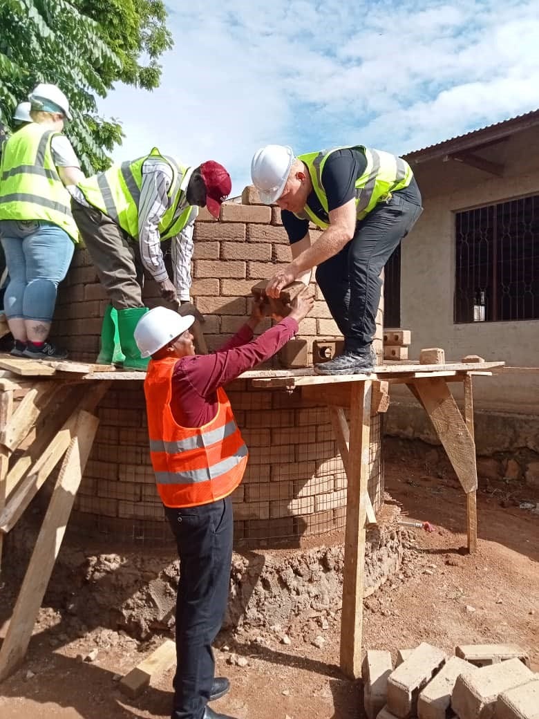 men working on scaffoding to cosntruct water tank with interlocking bricks