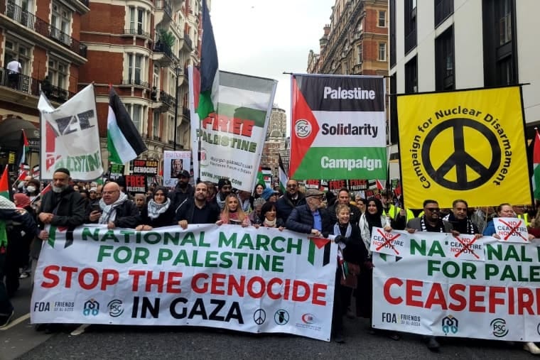 The front of the Palestine march in London, people hold three banners saying ceasefire now stop the genocide in Gaza