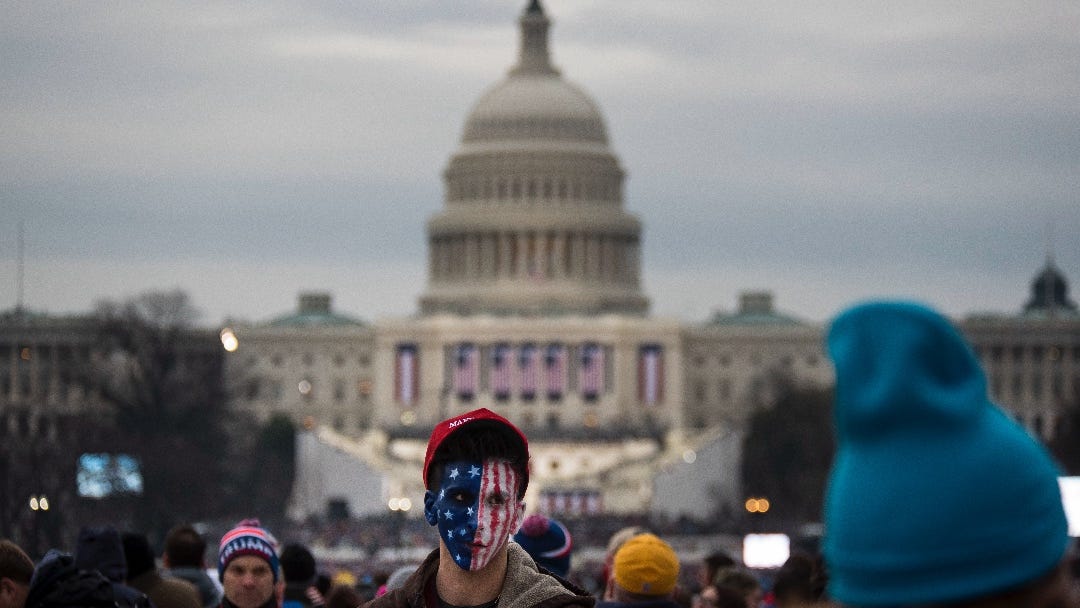 A young man with this face painted in the stars and stripes on the foreground, on the background the Capitol building