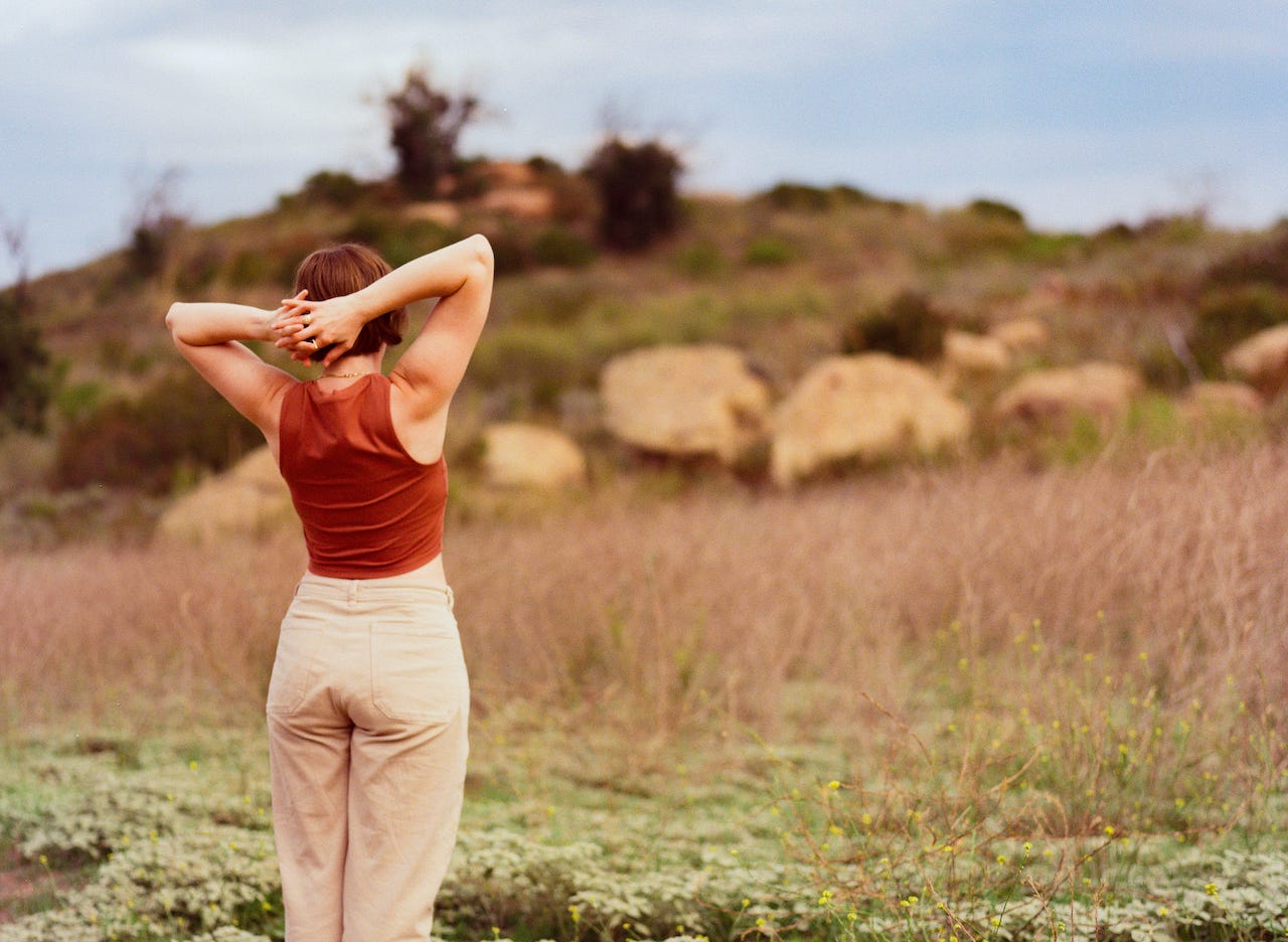 Image of Iris facing away from the camera with hands clasped behind their head looking into a field.