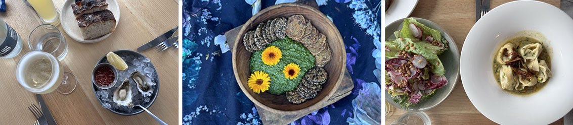A plate containing two oysters, another plate with bread and a glass of wine. A bowl with crackers, pesto and flowers, and two plates containing pasta and salad, respectively. A plate containing two oysters, another plate with bread and a glass of wine. A bowl with crackers, pesto and flowers, and two plates containing pasta and salad, respectively.