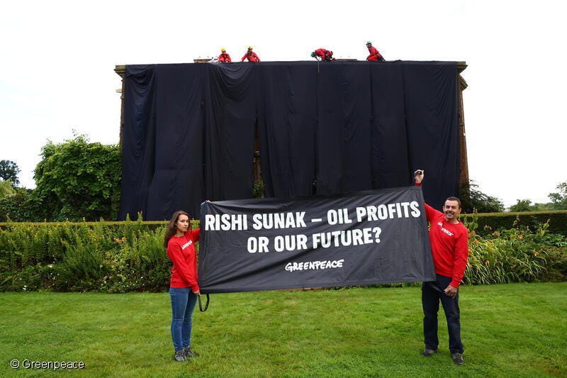 the PMs property covered in black cloths with two protestors holding a banner saying 'oil profits or our future'