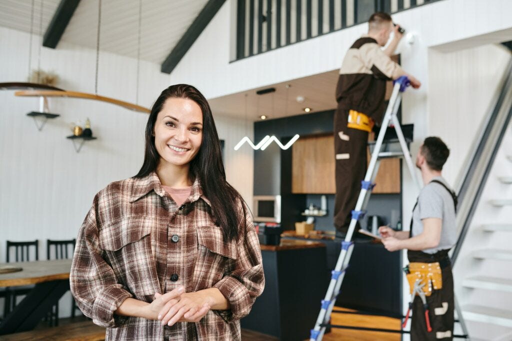 Young cheerful female standing against two repairmen working