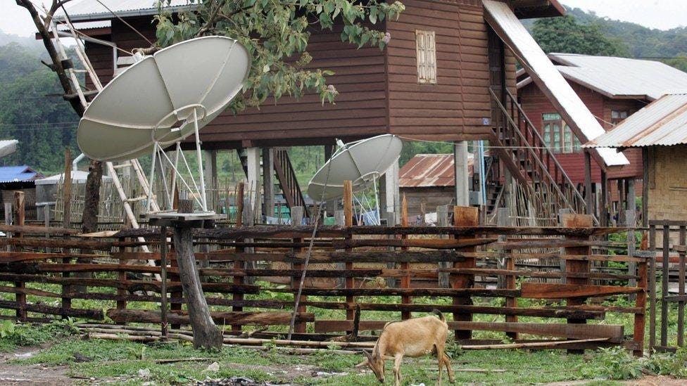 A goat eats grass near by TV satellite dishes installed outside houses at a village in the South-western Nakai plateau in Laos.