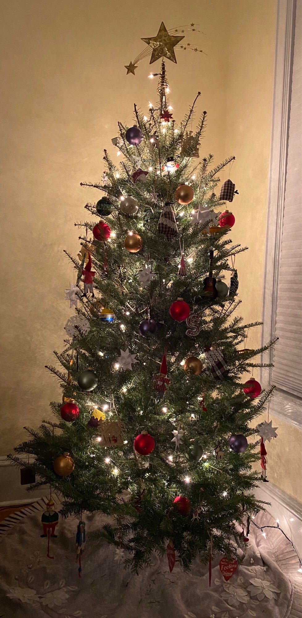 Green tree with shooting star tree topper, twinkly lights, and ornaments in corner of dim room.