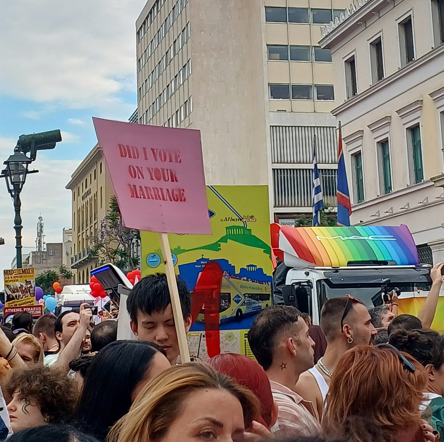 Uno scorcio della folla al Pride di Atene: una persona regge un cartello rosa che dice "Did I vote on your marriage?"
