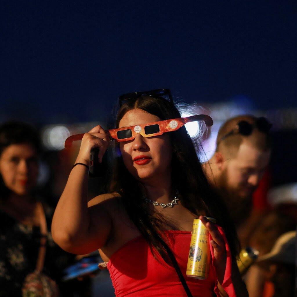 A woman wearing a red top holds protective glassed to her face in one hand and a yellow can in the other. 