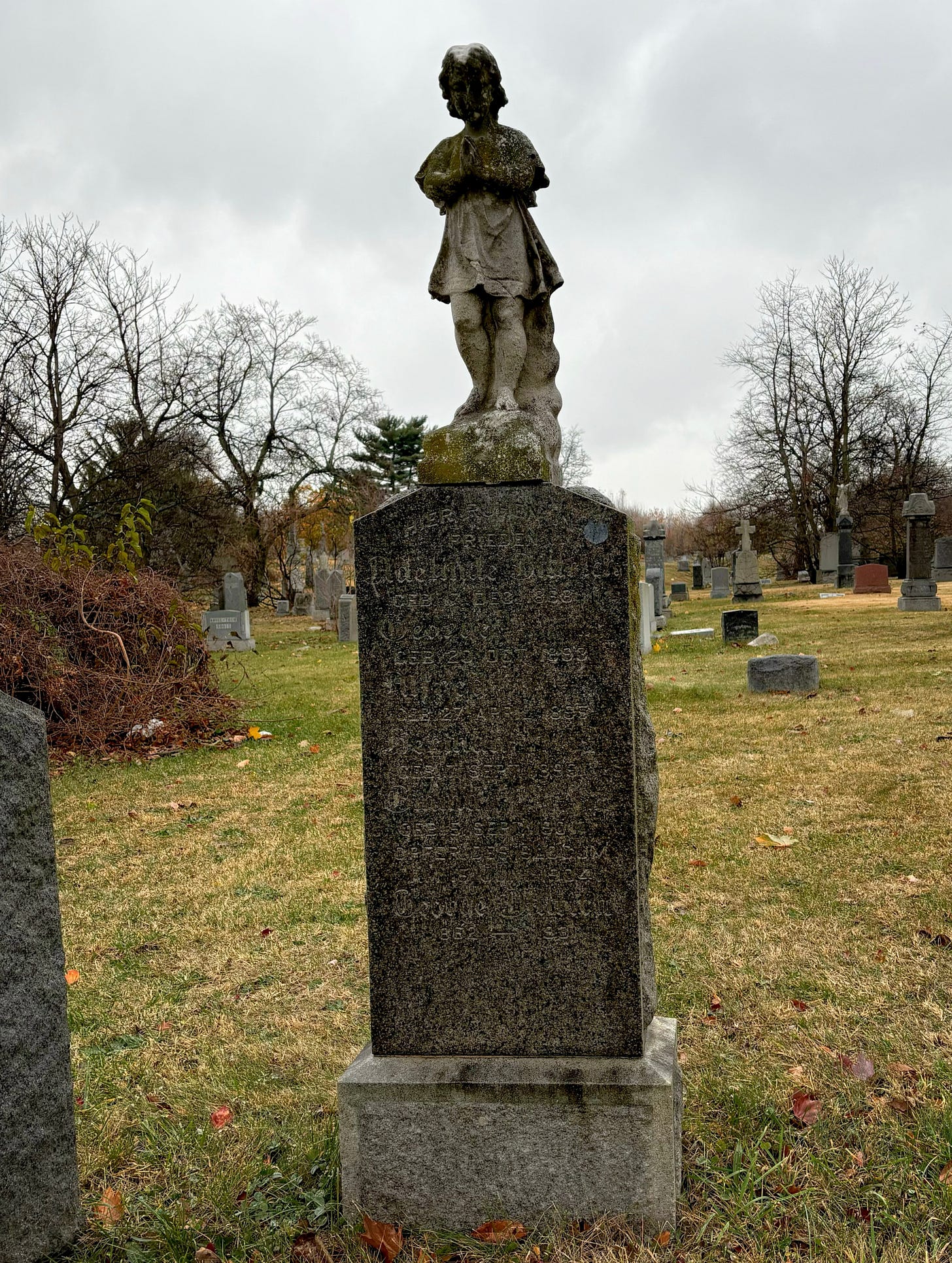 A monument of a child in prayer, eroded with age over the Dittrich family headstone.