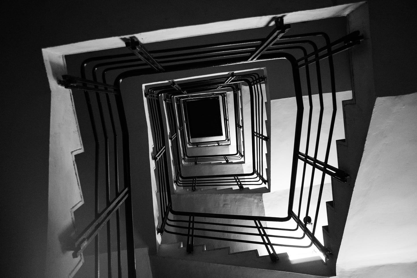 una tromba delle scale con ringhiera di metallo fotografata dal basso in bianco e nero