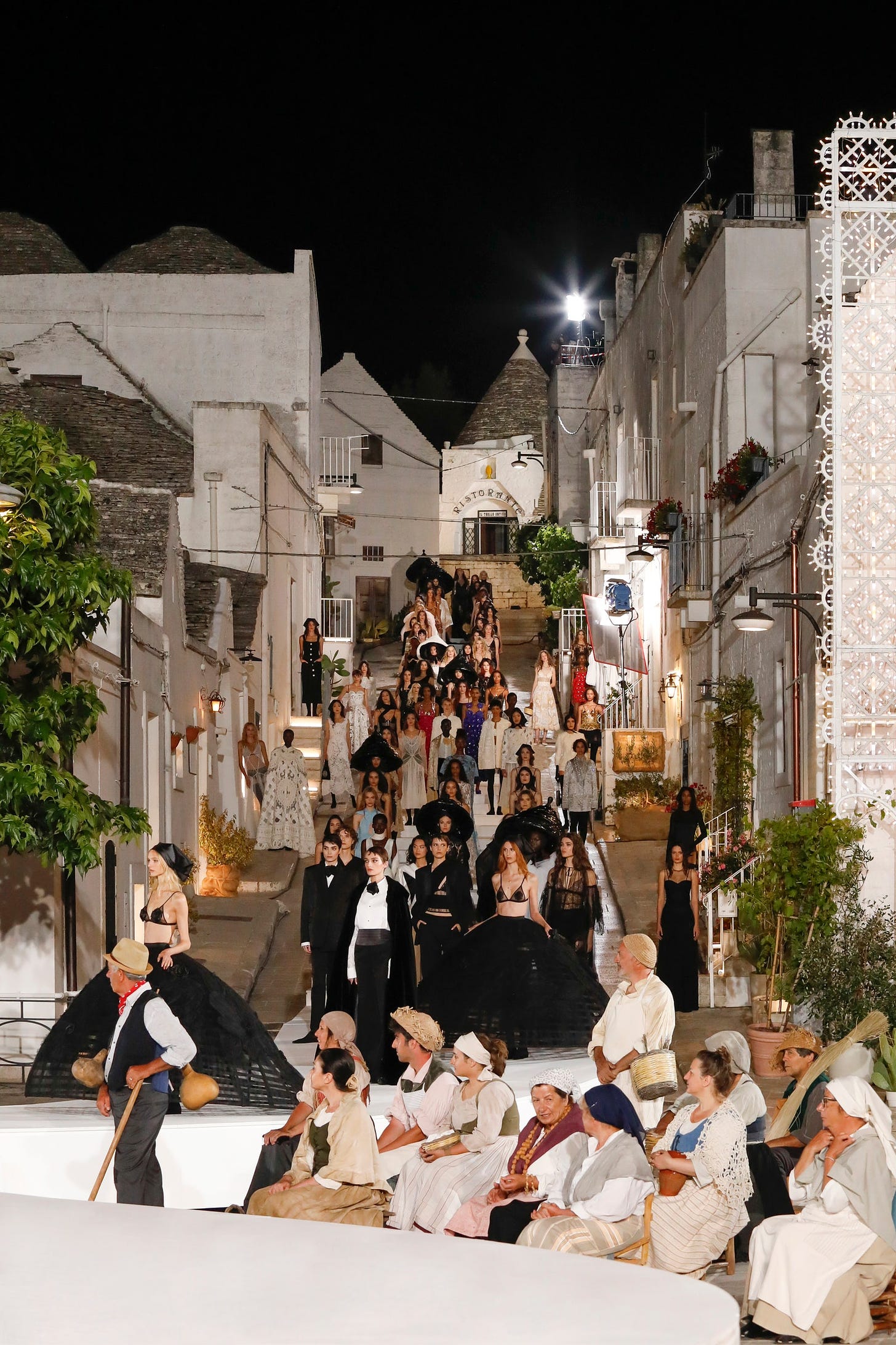 Models arrayed on a hilly street of Alberobello with local craftspeople looking on