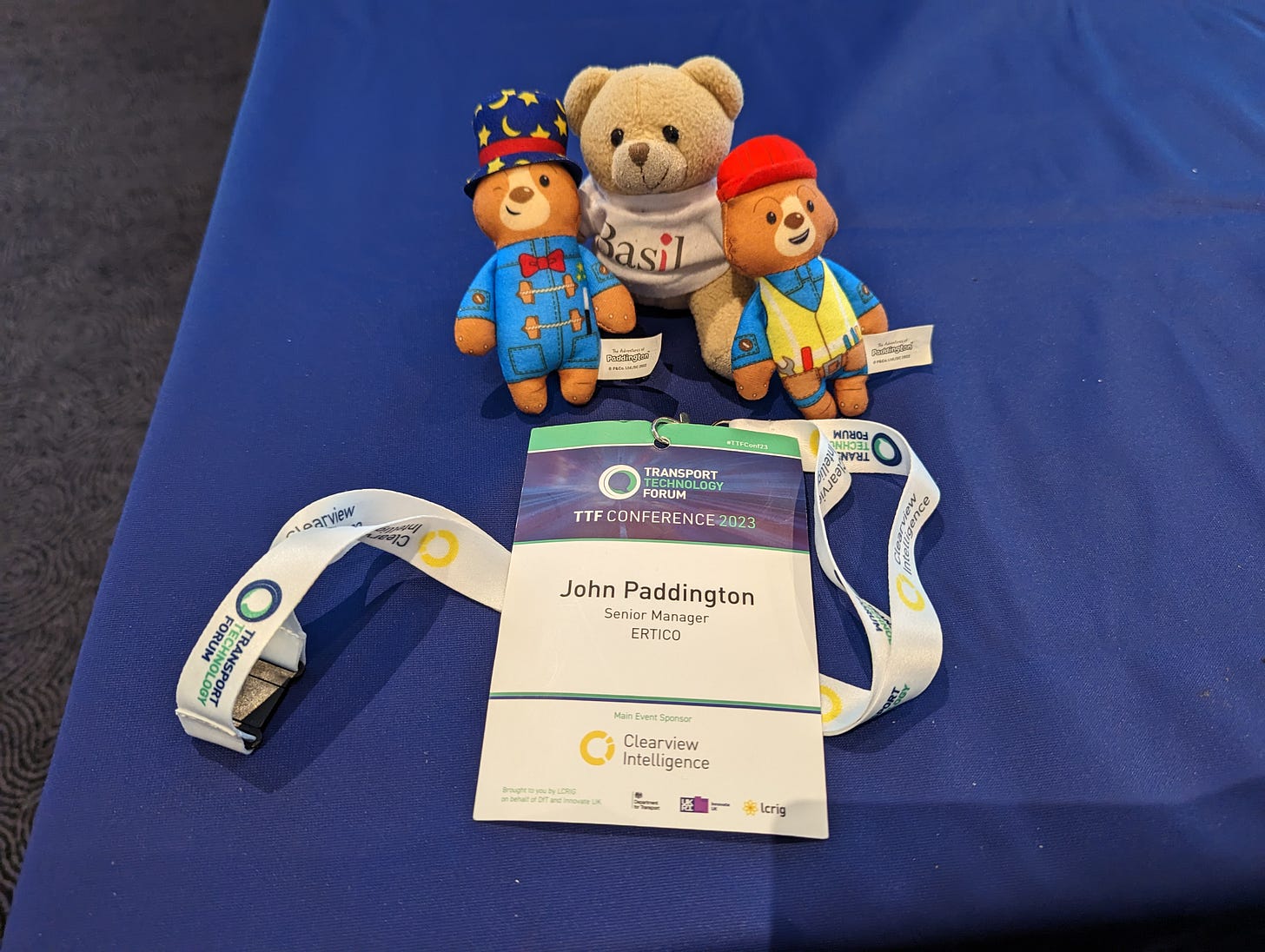 Photo of two Paddingtons (one with a magican hat and one wearing hi vis), Travel Basil teddy bear along with my conference badge