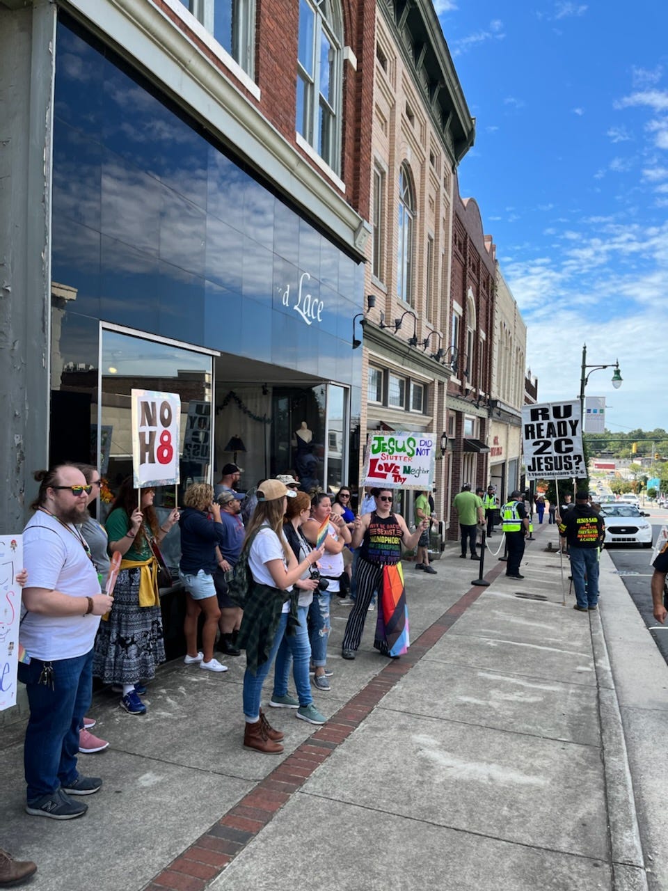 Image of pro-LGBTQIA+ local residents standing outside Tiffany’s restaurant against. One holds a sign that reads “No H8”