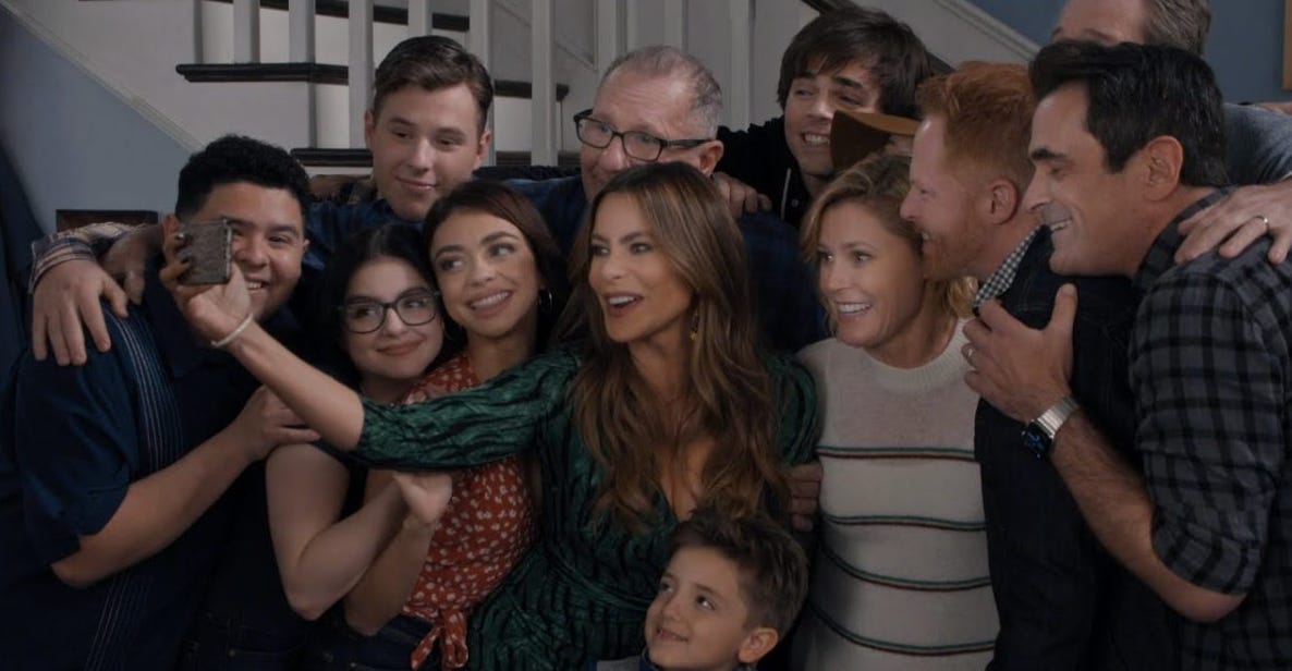 The characters of Modern Family lean in close to take a selfie together in a screenshot from the finale