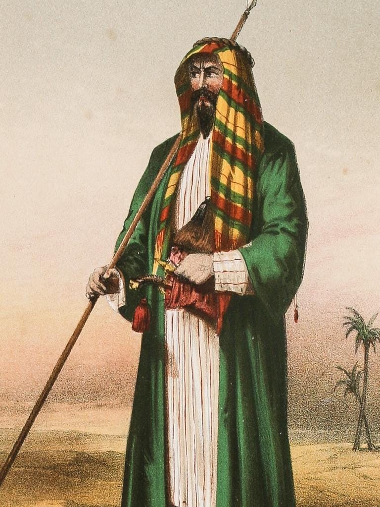 Man with fair skin and dark beard, clad in green robe, white thawb, and yellow, red, and green shemagh, carrying a long stick in his right hand. Palm trees and sand in background.