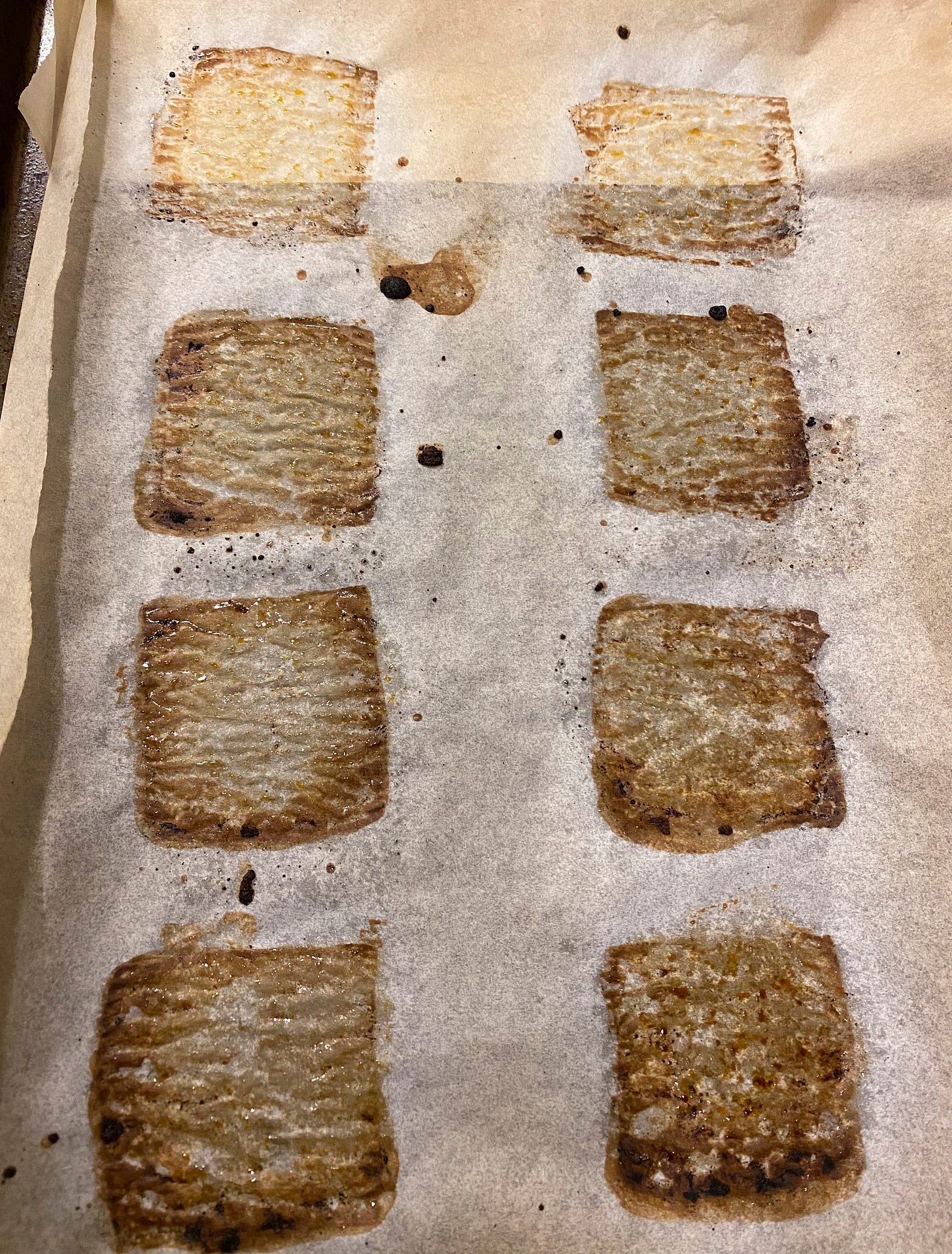 A piece of parchment paper stained dark in squares from baking the tofu. There are two columns of four squares each, and splashes of burned marinade around and between them.