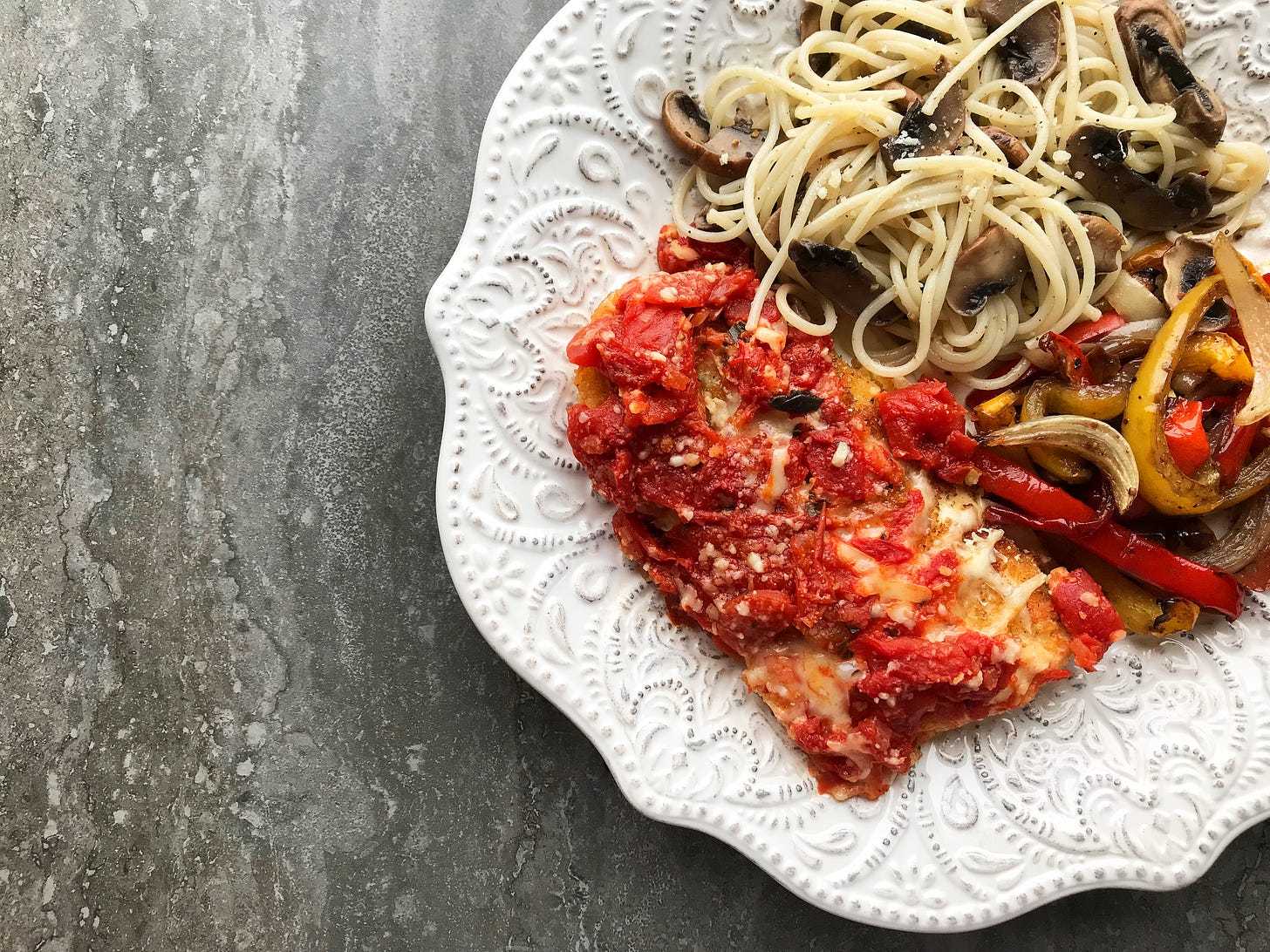 A plate of chicken parmesan with roasted peppers and pasta with mushrooms.
