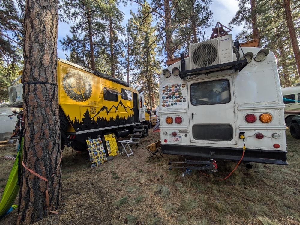 our yellow truck parked next to a large converted school bus in a campground with blue sky and pine trees