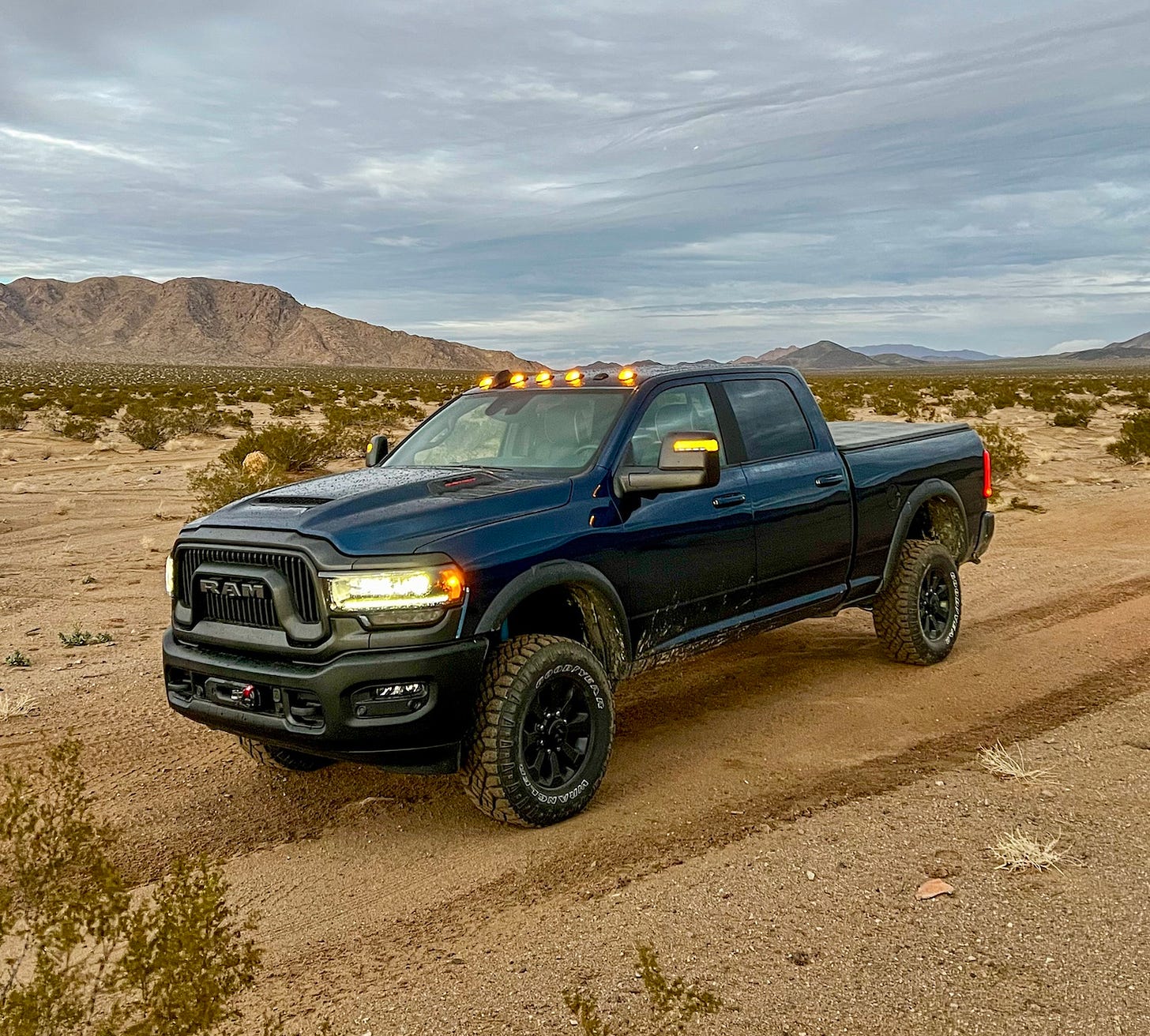 Front three-quarter view of a dark blue Ram 2500 Power Wagon parked in the desert, with dirt covering its all-terrain tires and splashed onto the doors.