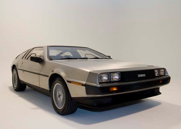 The image shows a silver-colored DeLorean DMC-12 sports car, a well-known vehicle from the "Back to the Future" movie franchise. The DeLorean is a distinctive, gull-wing door sports car with a stainless steel body. The image captures the car's unique and futuristic design, including its angular body shape and prominent front grille. The DeLorean is considered an iconic automobile from the 1980s and is often associated with time travel due to its prominent role in the "Back to the Future" movies.