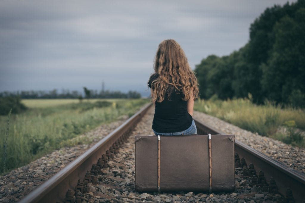 Portrait of young sad ten girl standing with suitcase outdoors a
