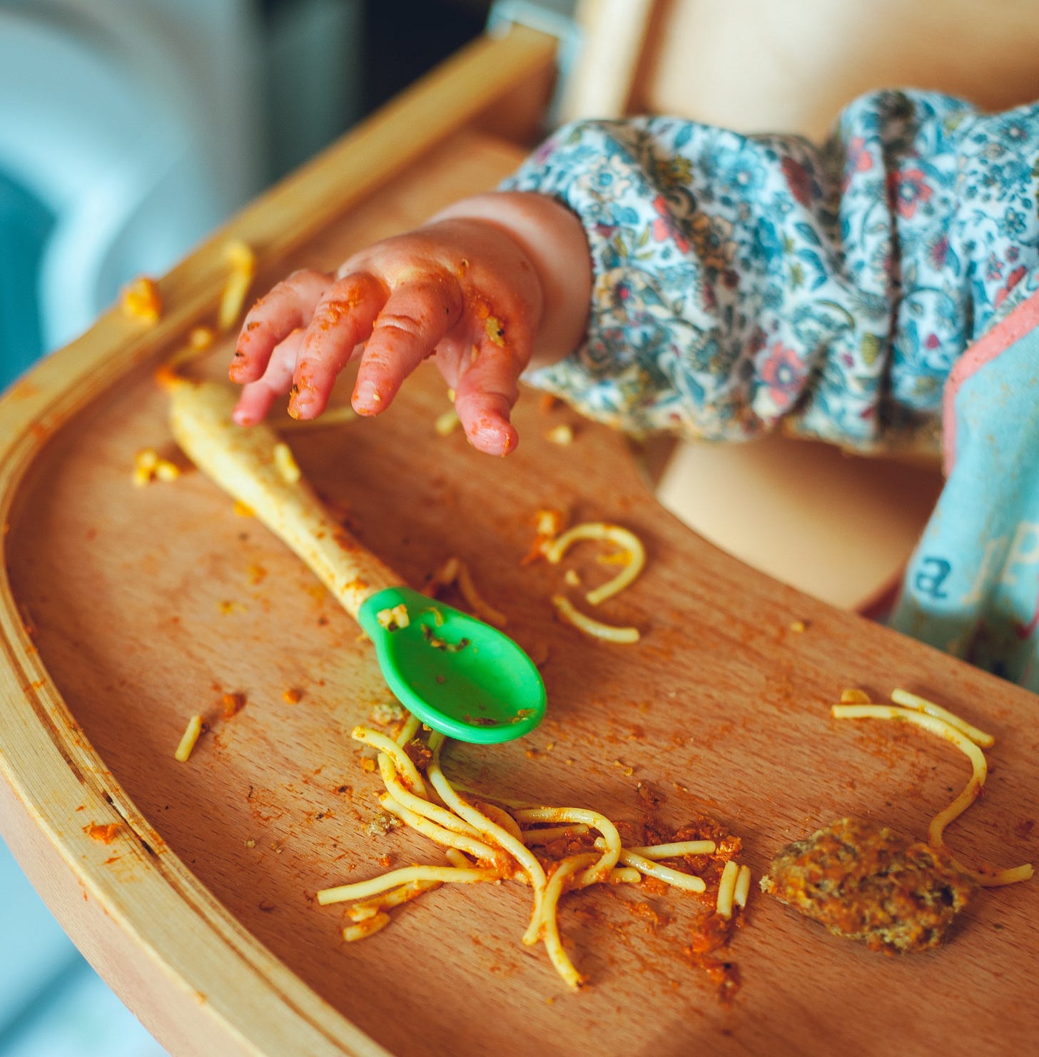 A child sitting in a highchar, with what looks like spaghetti bolognese thrown around the tray and covering the child's hand A child sitting in a highchar, with what looks like spaghetti bolognese thrown around the tray and covering the child's hand