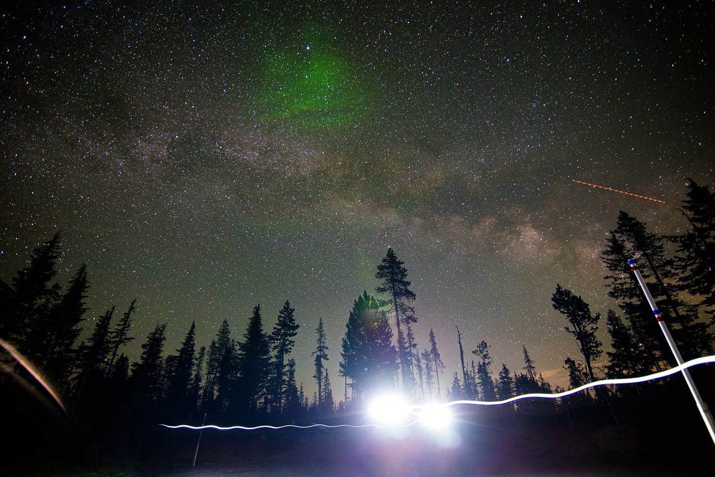 Milky Way sky with a forested foreground, streaks of a light from someone with a headlamp