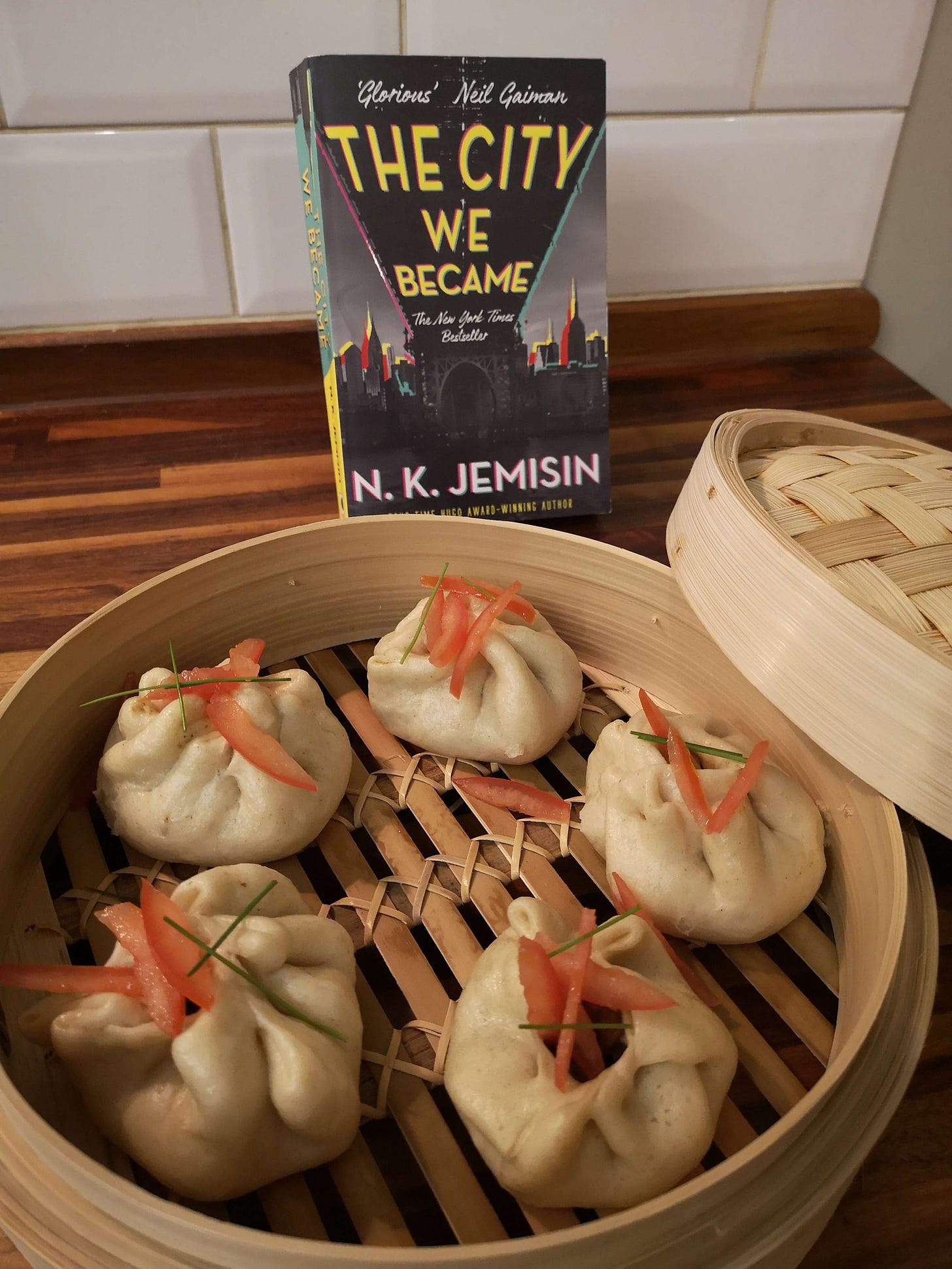 Delicious looking dumplings sitting in a bamboo steamer in front of N.K. Jemisin's "The City We Became."