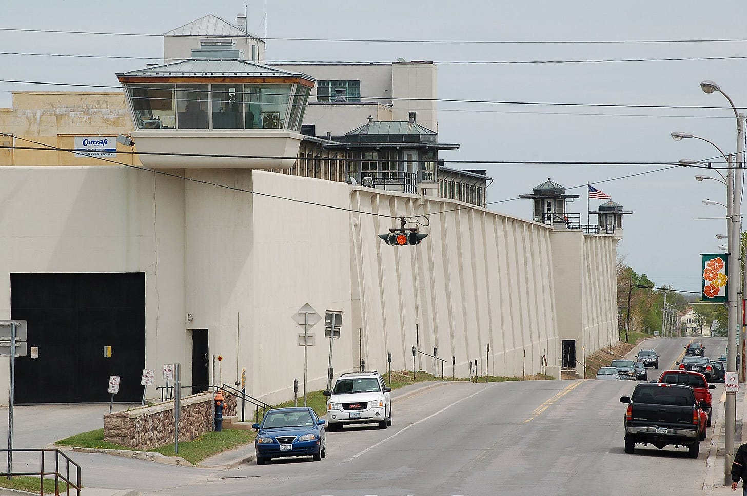 a prison and the road outside it, with cars; prison has guard towers a prison and the road outside it, with cars; prison has guard towers