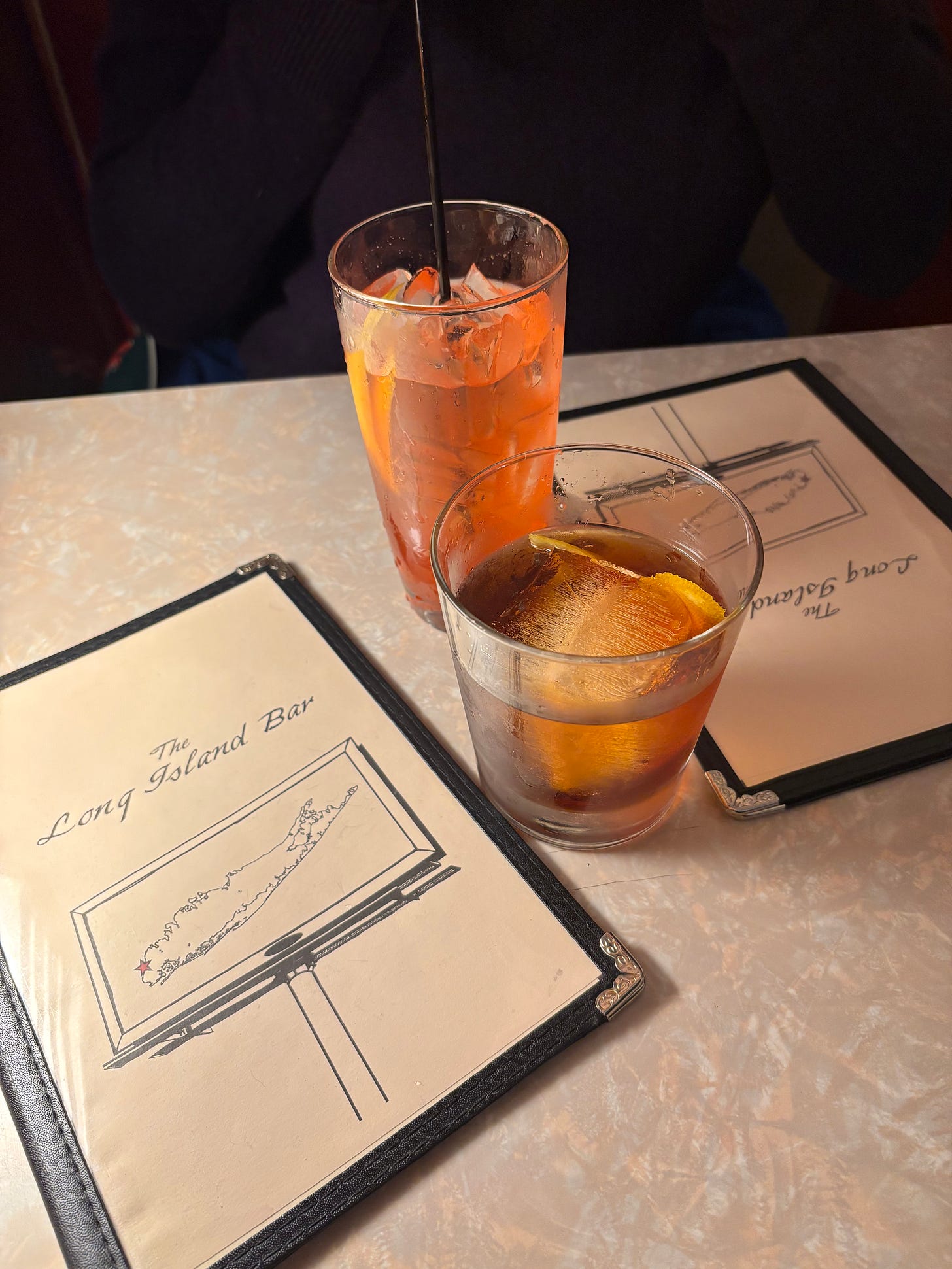 A collins glass and rocks glass sitting on a table, flanked by menus labelled "The Long Island Bar"