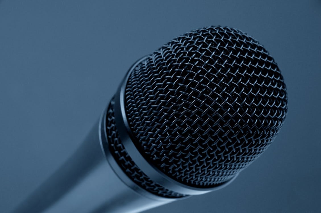 Free A detailed close-up of a microphone with a blue monochrome background, highlighting its intricate mesh design. Stock Photo