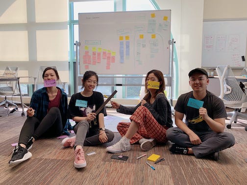 A group of 4 CMU students sitting on carpet with sticky notes, rulers, and pens.
