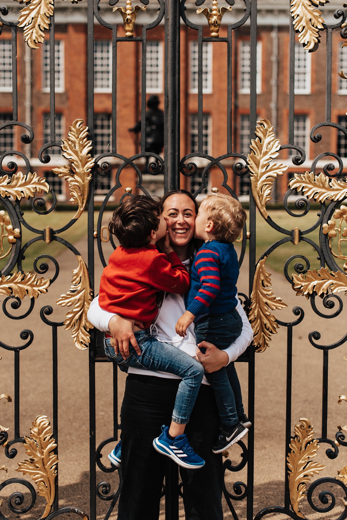 Andrea Caamano standing outside Kensington Palace holding her two children