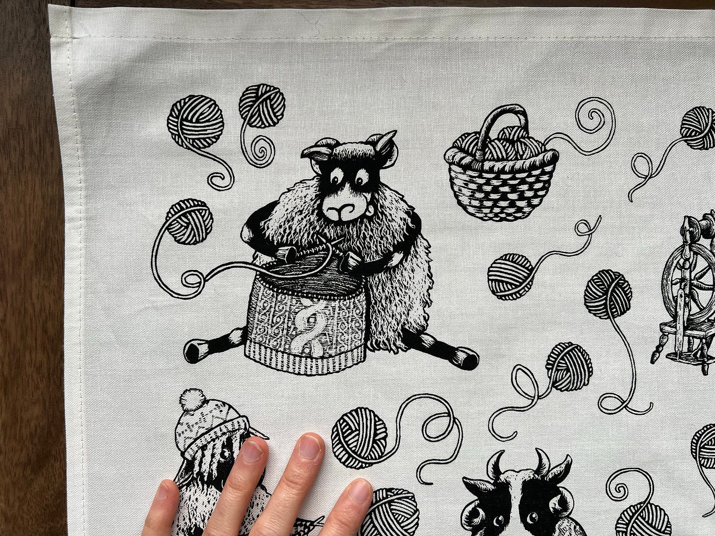 A close up of an illustrated tea towel. A Sheep works on a cable knit jumper