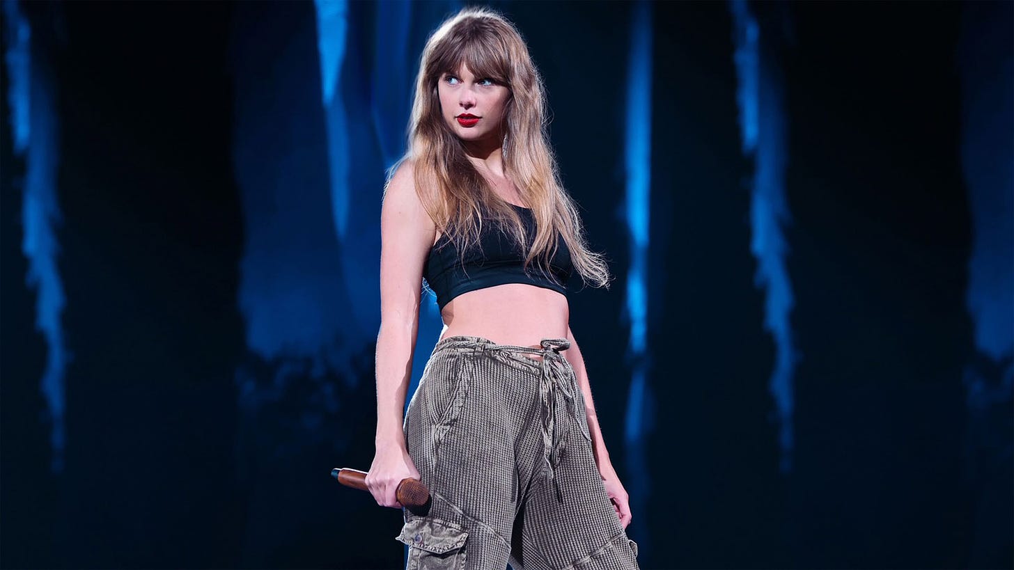 Foto de Taylor Swift en un concierto. Se la ve con pose segura y sujetando un micro marrón.